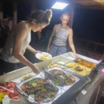 Guests serving BBQ dinner on deck during the Musandam overnight dhow cruise